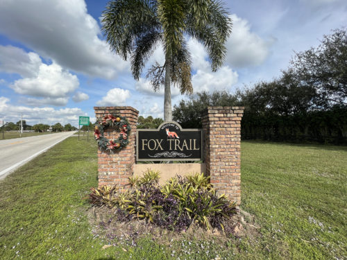Road in backdrop behind the fox trail entrance sign leading into this Loxahatchee fl community